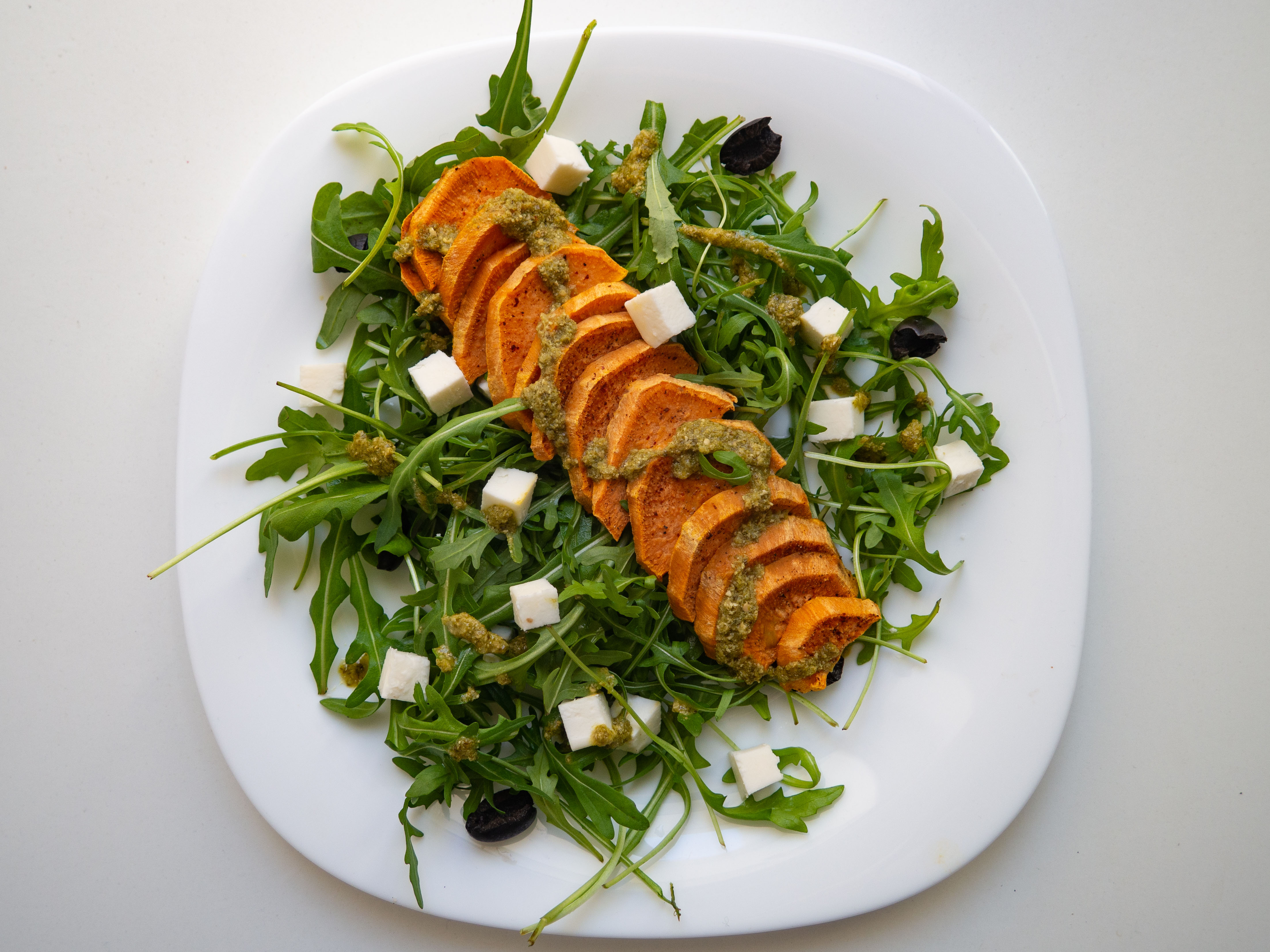 Sweet potatoes with feta cheese and pesto on rocket